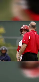 Softball player and coach in red talking on field with helmet.