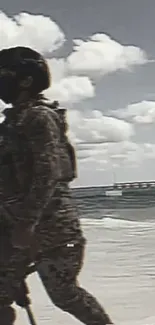 A soldier in camouflage walks along a beach under a cloudy sky.