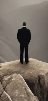 Lone man stands on a rocky peak overlooking a misty mountainous landscape.