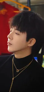 Man in black attire with gold necklaces, side profile.