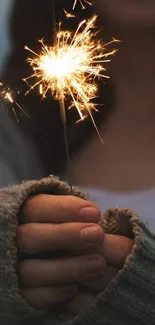 A close-up of hands holding a glowing sparkler in a cozy, dark setting.