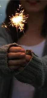 A cozy hand holds a brightly lit sparkler in a soft, textured sweater against a dark backdrop.