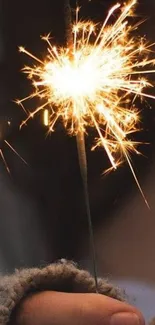 A warm orange sparkler glowing brightly in a person's hand.