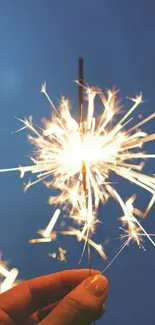 Hand holding a sparkler against a blue sky at night.