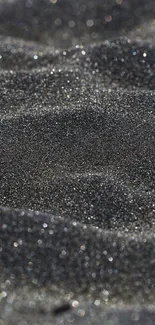 Close-up of sparkling black sand texture with dark tones.
