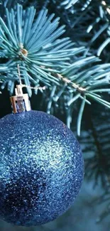 Sparkling blue ornament hanging on pine branch with festive glitter.