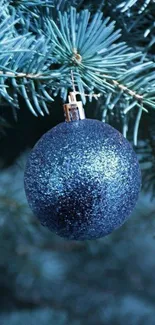 A glittering blue ornament hangs on a festive pine tree branch.