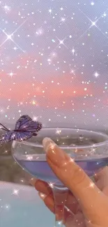 Hand holding a glass with a butterfly against a sparkling sunset.