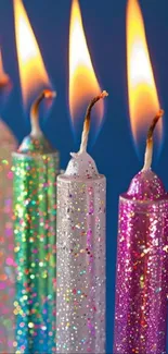 Glitter-covered birthday candles with bright flames on a blue background.