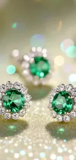 Elegant sparkling emerald earrings on a shimmering gold background.