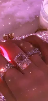 Glamorous hand with diamond rings on a sparkling pink backdrop.