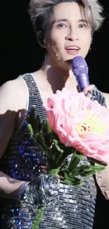 Performer holding pink flower on stage with shimmering outfit, striking image.