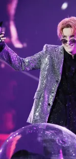 Performer in sequined jacket with microphone on purple-lit stage.