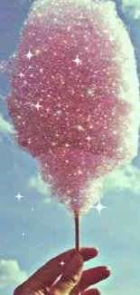 Hand holding sparkling pink cotton candy against a bright blue sky.