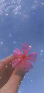 Hand holding a pink flower against a sparkling blue sky with stars.