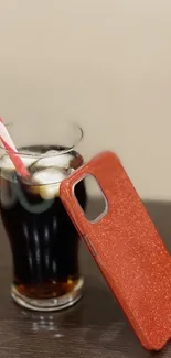 Red glitter phone case with iced drink on wooden table.