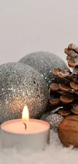 A silver ornament, candle, and pinecone on snow.