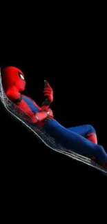 Superhero lounging in web hammock on phone, black background.