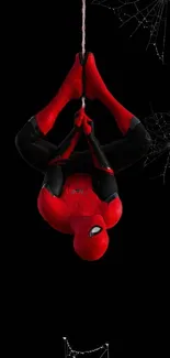 Spider-Man hanging upside down on a web with black background.