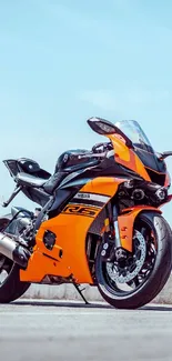 Orange sport bike on open road under blue sky.