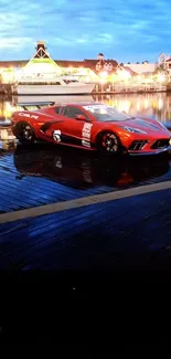 Red sports car at night by a waterfront marina.