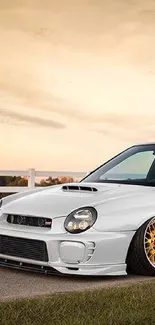 White sports car with gold wheels against a sunset backdrop.