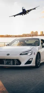 White sports car on highway with jet plane overhead.