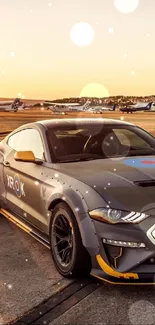 Grey sports car parked at sunset near airplanes.