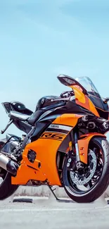 Vibrant orange sport motorcycle on pavement under blue sky.