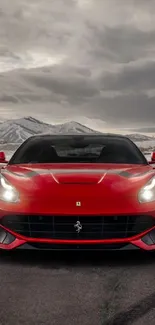 Red sports car on road with mountains and cloudy sky backdrop.