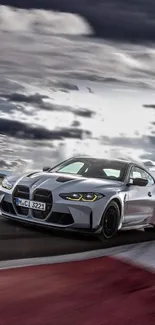 Sleek silver sports car racing under a dramatic sky on a track.