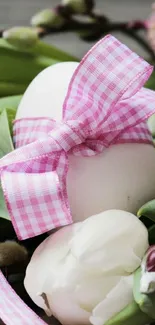 White egg with pink ribbon among tulips and leaves.