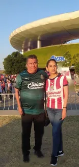 Two fans in sporty outfits outside a stadium.