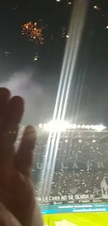 Hand raised under stadium fireworks at night.