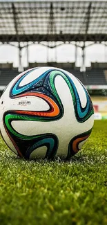 Soccer ball on green field with stadium backdrop.