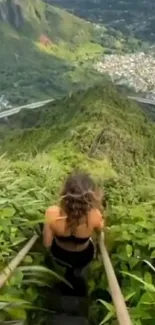 Woman climbs lush mountain stairs with city view.