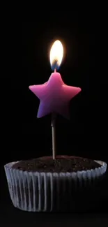 Pink star candle on a chocolate cupcake against a dark backdrop.