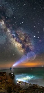 Person stands on rocks under the Milky Way and starry sky by the seaside.