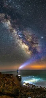 Person stargazing at the Milky Way over a rocky coast under a vibrant night sky.