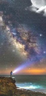 Starry night sky over the ocean with Milky Way and a person holding a flashlight.