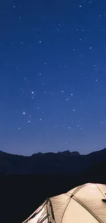 Camp under a starry sky with tent and mountains in view.