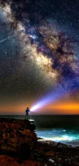 Milky Way over ocean with silhouetted figure holding flashlight.