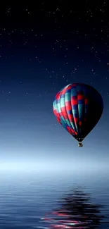 Starry night with hot air balloon over serene water reflection.