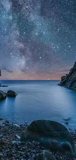 Starry night sky over a calm beach with rocky shoreline.