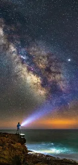 Stargazer with flashlight under a starry galaxy sky by the ocean.