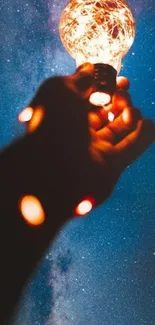 Hand holding glowing lamp against starry night sky.