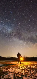 Silhouette under a starry night sky with lantern on a dark landscape.