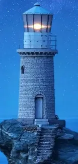 Lighthouse under a starry blue night sky on rocky cliffs.