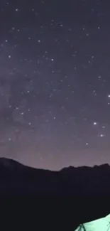 Starry night sky over mountains with a glowing tent.