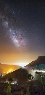 Starry night sky over a lit mountain landscape.